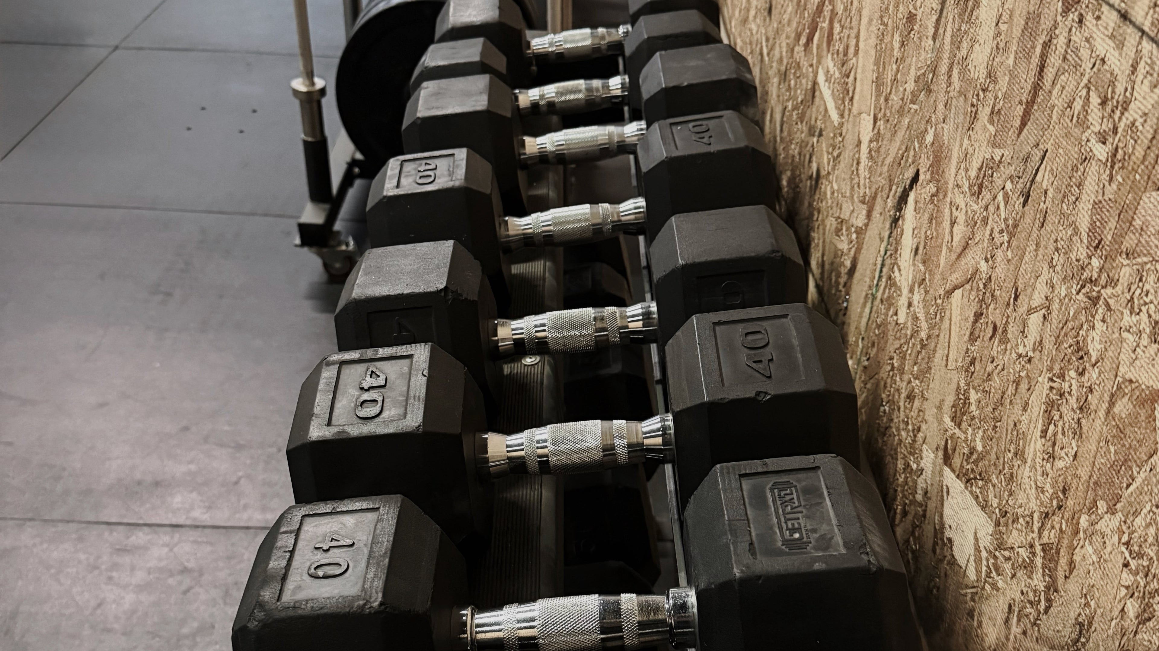 Row of hexagonal dumbbells on a rack against a wooden wall.